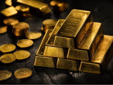 Gold bars and coins on a dark stone surface